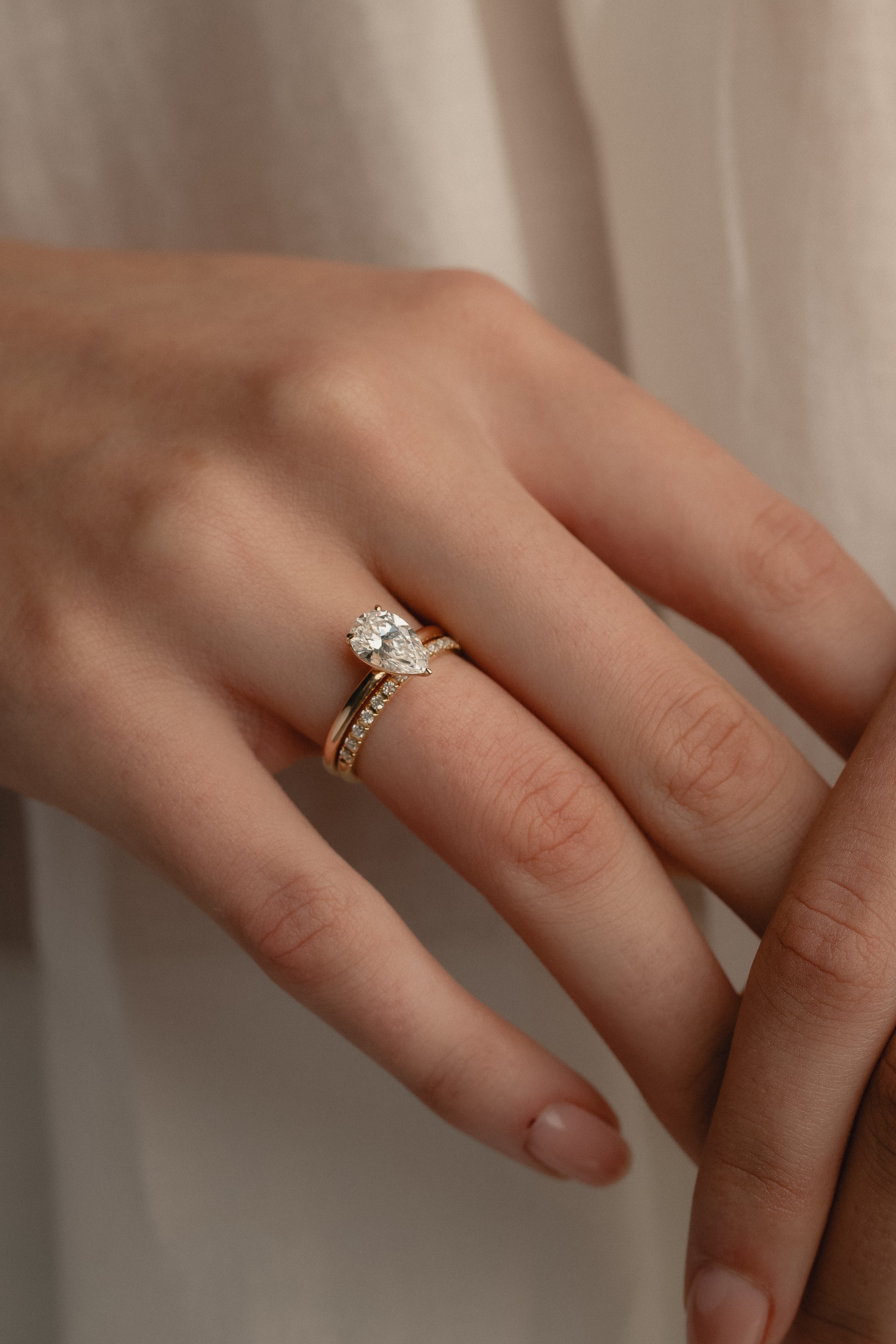A detailed macro view of a rose gold KARAAT pear-cut solitaire diamond engagement ring paired flawlessly with a sparkling pavé diamond wedding band on a model's hand.