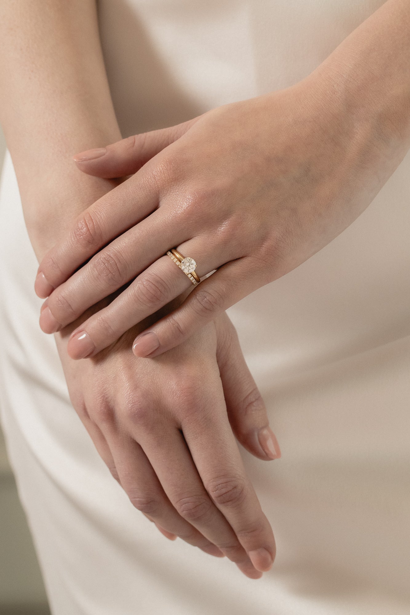 A model wearing a KARAAT Round Solitaire paired with a matching 18k yellow gold wedding band against a silk wedding dress.
