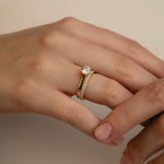 A soft-focus luxury bridal shot of a model's hand displaying a brilliant round solitaire diamond engagement ring nested flush beside the statement Pavé Diamond Ring III on a classic yellow gold band.