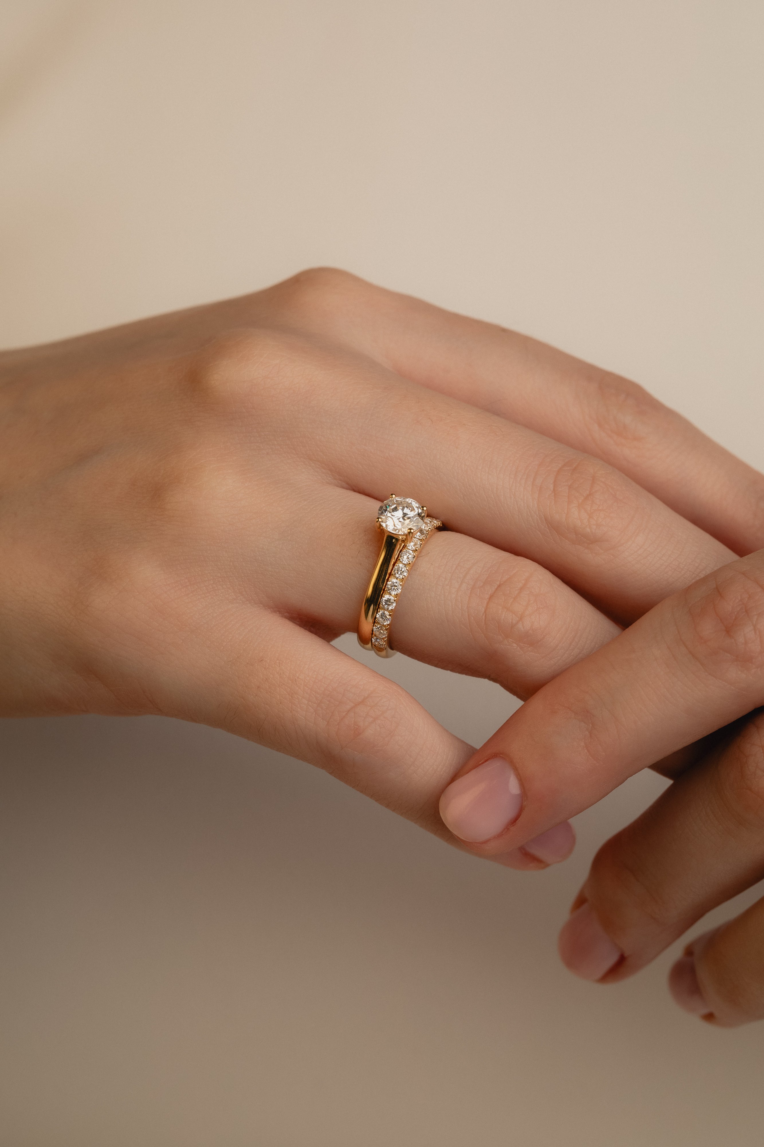 A soft-focus luxury bridal shot of a model's hand displaying a brilliant round solitaire diamond engagement ring nested flush beside the statement Pavé Diamond Ring III on a classic white gold band.