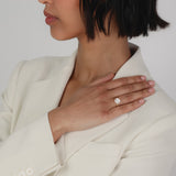 An elegant side profile of a bridal model wearing a tailored cream blazer, showcasing a KARAAT round solitaire diamond engagement ring with a brilliant halo setting on her finger.