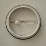 A flat-lay, top-down photograph of a rose gold KARAAT round solitaire halo diamond engagement ring paired with a matching sparkling diamond wedding band, perfectly nestled side-by-side inside a round taupe velvet ring box.