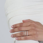 Close-up of a model wearing a crisp white top with her hands folded, elegantly displaying a modern three-layer ring stack composed of fine yellow gold KARAAT pavé diamond wedding bands.